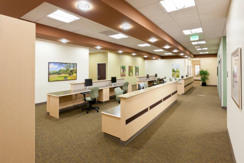 A modern administrative workstation area in a healthcare facility features multiple desks, office chairs, warm lighting, and framed artwork on the walls, creating a professional and welcoming atmosphere. - Total Health Environment