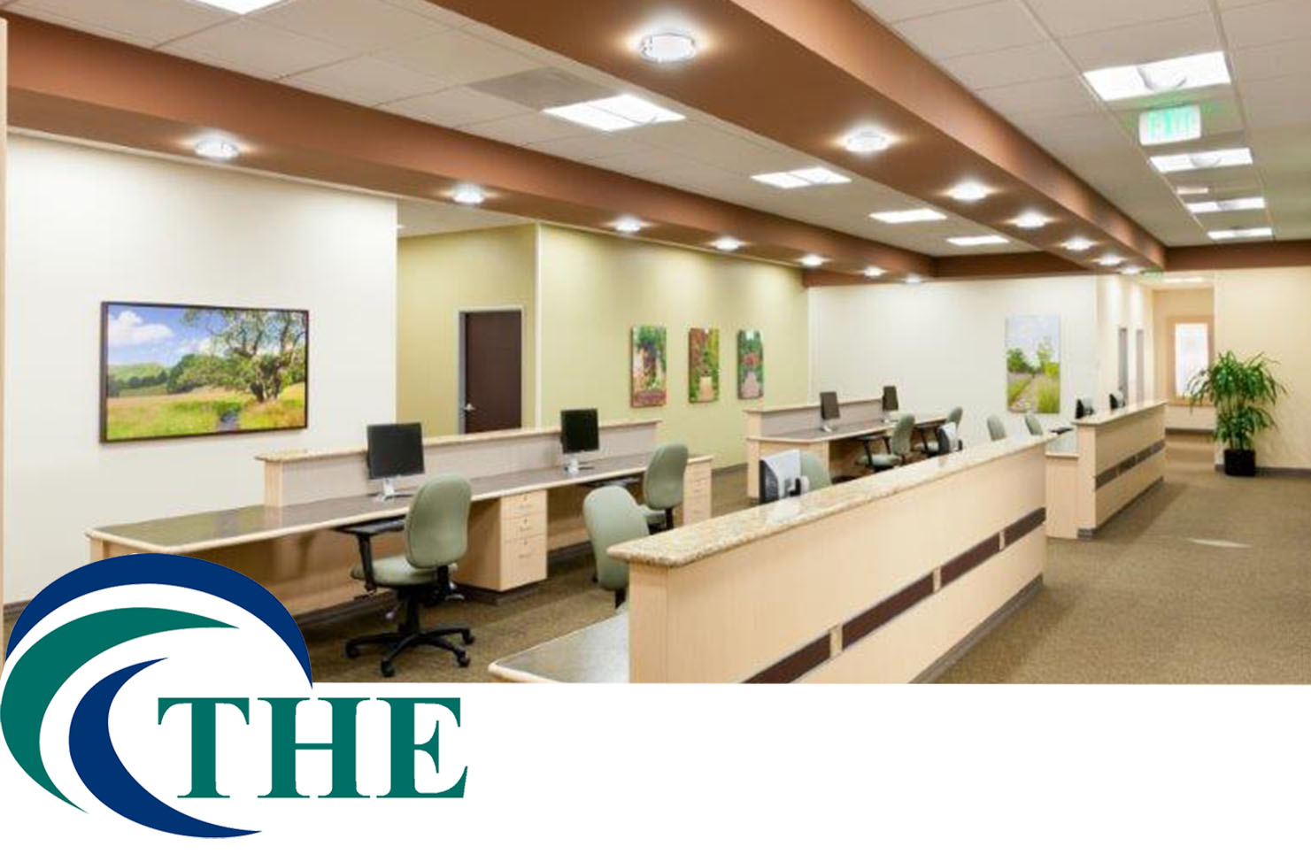 A spacious and well-lit medical office reception area featuring a long front desk, multiple workstations, framed landscape artwork, and a logo in the bottom left corner reading "THE" for Total Health Environment. - Total Health Environment