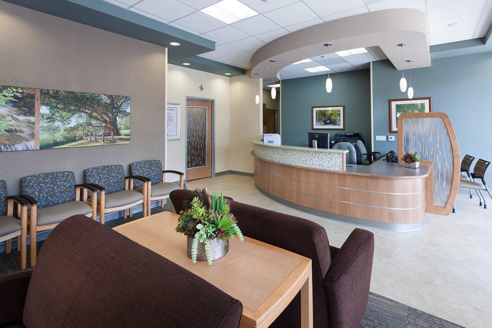 A spacious and inviting medical waiting area features comfortable seating, a curved reception desk, warm lighting, and decorative elements, creating a welcoming healthcare environment. - Total Health Environment